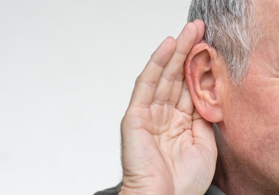 Man gesturing to his ear to indicate he can't hear